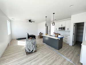 Kitchen with hanging light fixtures, light wood-type flooring, white cabinets, and a kitchen island