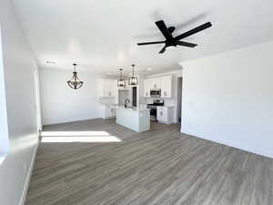 Unfurnished living room featuring hardwood / wood-style floors, ceiling fan with notable chandelier, and sink