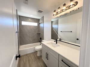 Full bathroom with toilet, tiled shower / bath, wood-type flooring, a textured ceiling, and vanity