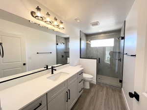 Bathroom with hardwood / wood-style floors, vanity, toilet, a shower with door, and a textured ceiling