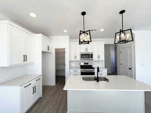 Kitchen with appliances with stainless steel finishes, sink, pendant lighting, and a kitchen island with sink