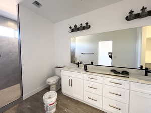 Bathroom featuring vanity, wood-type flooring, toilet, and a tile shower