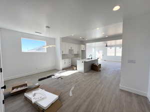 Unfurnished living room with ceiling fan, sink, light hardwood / wood-style flooring, and a wealth of natural light