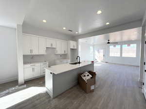 Kitchen featuring sink, light hardwood / wood-style flooring, a kitchen island with sink, backsplash, and white cabinets