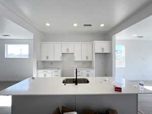 Kitchen featuring white cabinetry, sink, tasteful backsplash, and a large island with sink