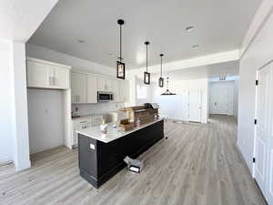 Kitchen with decorative light fixtures, light hardwood / wood-style flooring, a center island, and white cabinets