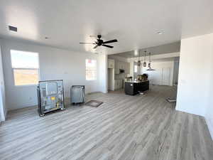 Interior space with a textured ceiling, ceiling fan, and light hardwood / wood-style flooring