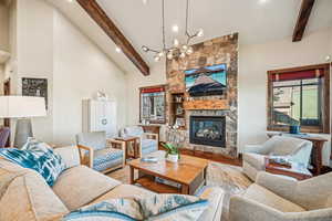 Living room featuring beamed ceiling, an inviting chandelier, high vaulted ceiling, hardwood / wood-style floors, and a stone fireplace