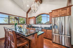 Kitchen with a kitchen island, stainless steel appliances, a notable chandelier, dark stone counters, and dark hardwood / wood-style flooring