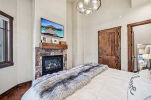 Bedroom with a stone fireplace, hardwood / wood-style flooring, and a chandelier