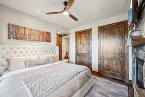 Bedroom featuring wood-type flooring, a stone fireplace, two closets, and ceiling fan