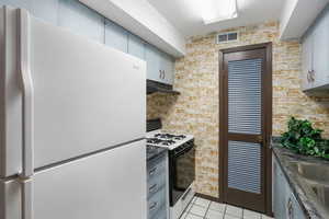 Kitchen with white appliances, sink, light tile patterned floors, and brick wall