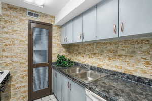 Kitchen with brick wall, light tile patterned floors, sink, and electric range