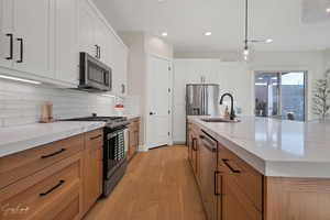 Kitchen featuring a large island with sink, white cabinetry, stainless steel appliances, light hardwood / wood-style flooring, and sink