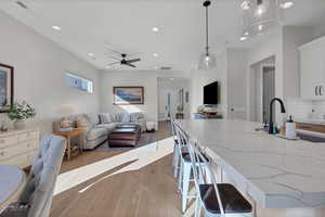 Kitchen with pendant lighting, light stone countertops, tasteful backsplash, white cabinetry, and light wood-type flooring