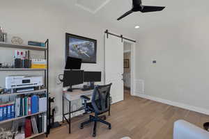 Office area featuring a barn door, light wood-type flooring, and ceiling fan