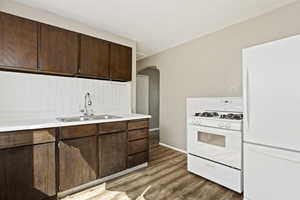 Kitchen featuring dark brown cabinetry, light hardwood / wood-style floors, sink, and white appliances