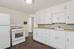 Kitchen with white cabinets, sink, white appliances, a textured ceiling, and dark hardwood / wood-style floors