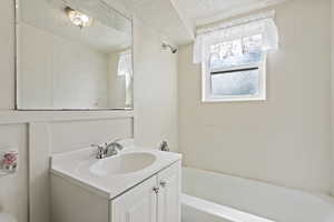 Bathroom with a textured ceiling, vanity, and bathtub / shower combination