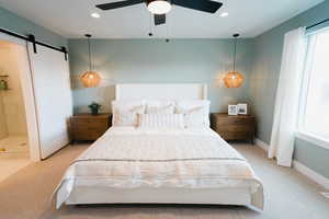 Carpeted bedroom featuring ensuite bath, ceiling fan, and a barn door