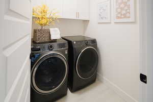 Laundry area with washing machine and dryer, light tile patterned floors, and cabinets