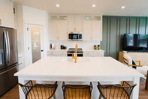 Kitchen with appliances with stainless steel finishes, a center island with sink, white cabinetry, and dark hardwood / wood-style flooring