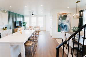 Kitchen featuring light hardwood / wood-style floors, sink, ceiling fan with notable chandelier, white cabinetry, and a kitchen bar