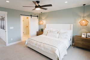 Bedroom featuring light carpet, connected bathroom, ceiling fan, and a barn door