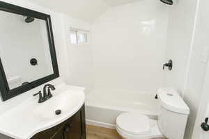 Full bathroom featuring hardwood / wood-style flooring, lofted ceiling, tiled shower / bath combo, vanity, and toilet