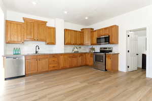 Kitchen with light hardwood / wood-style floors, appliances with stainless steel finishes, backsplash, and sink