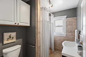 Bathroom with tile walls, a shower with shower curtain, tile patterned floors, vanity, and toilet