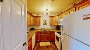 Kitchen featuring sink, hanging light fixtures, an inviting chandelier, white appliances, and dark hardwood / wood-style flooring