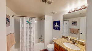 Full bathroom featuring shower / bath combination with curtain, a textured ceiling, vanity, and toilet