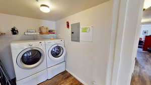 Clothes washing area featuring a textured ceiling, dark hardwood / wood-style floors, electric panel, and separate washer and dryer