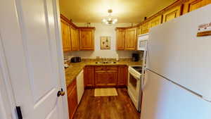 Kitchen featuring dark hardwood / wood-style floors, sink, an inviting chandelier, white appliances, and decorative light fixtures