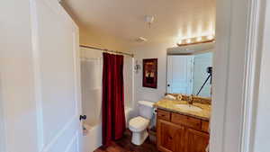 Full bathroom with shower / bath combination with curtain, a textured ceiling, hardwood / wood-style floors, vanity, and toilet