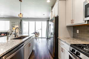 Kitchen with white cabinets, hanging light fixtures, sink, appliances with stainless steel finishes, and dark hardwood / wood-style floors