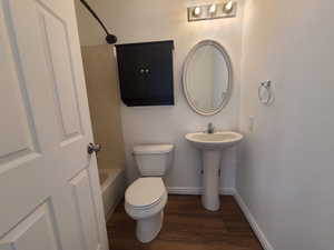 Hall bath with toilet, a sink, wood laminate floors, and tub / shower combination