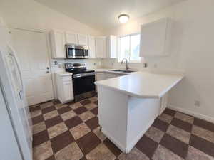 Kitchen with sink, white cabinets, vaulted ceiling, peninsula, and stainless steel appliances