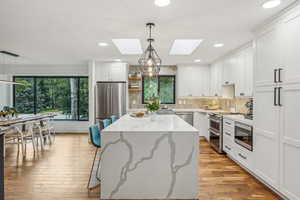 Kitchen with pendant lighting, a center island, white cabinetry, stainless steel appliances, and a skylight