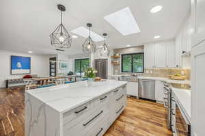 Kitchen featuring a wealth of natural light, a skylight, stainless steel appliances, and white cabinets