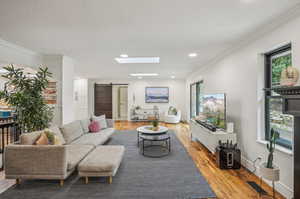 Living room featuring light hardwood / wood-style flooring, a skylight, crown molding, and a barn door