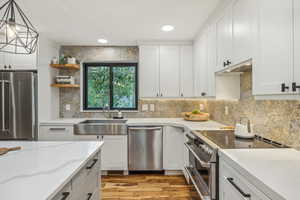 Kitchen featuring white cabinets, stainless steel appliances, light wood-type flooring, decorative light fixtures, and sink