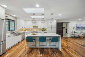 Kitchen with wood-type flooring, a center island, white cabinetry, a barn door, and appliances with stainless steel finishes