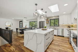 Kitchen with premium appliances, decorative backsplash, light wood-style floors, a skylight, and white cabinets