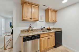 Kitchen with light stone counters, light brown cabinets, sink, and stainless steel dishwasher