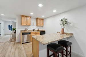 Kitchen with light stone counters, dishwasher, light brown cabinetry, a breakfast bar area, and light wood-type flooring