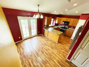 Kitchen with light wood-type flooring, stainless steel range with electric cooktop, vaulted ceiling, kitchen peninsula, and hanging light fixtures