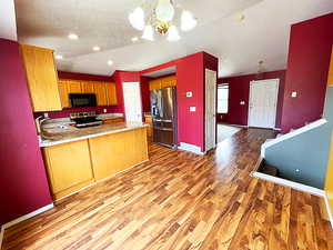 Kitchen with light hardwood / wood-style floors, vaulted ceiling, kitchen peninsula, stainless steel appliances, and decorative light fixtures