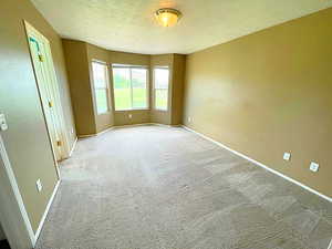 Empty room with a textured ceiling and light colored carpet